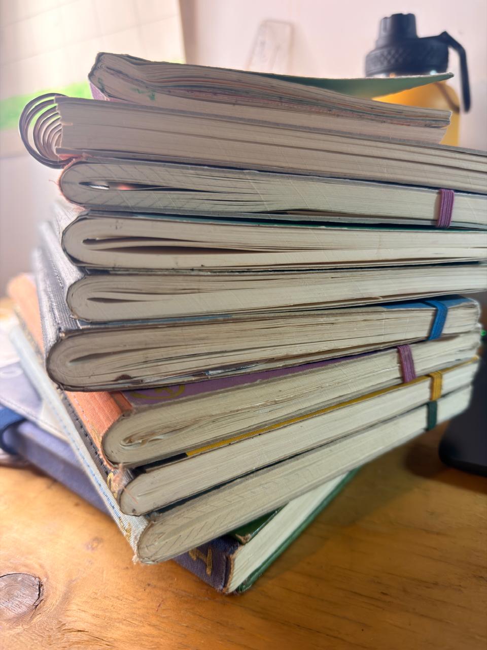 Pilha de cadernos manuscritos e gastos sobre uma mesa de madeira