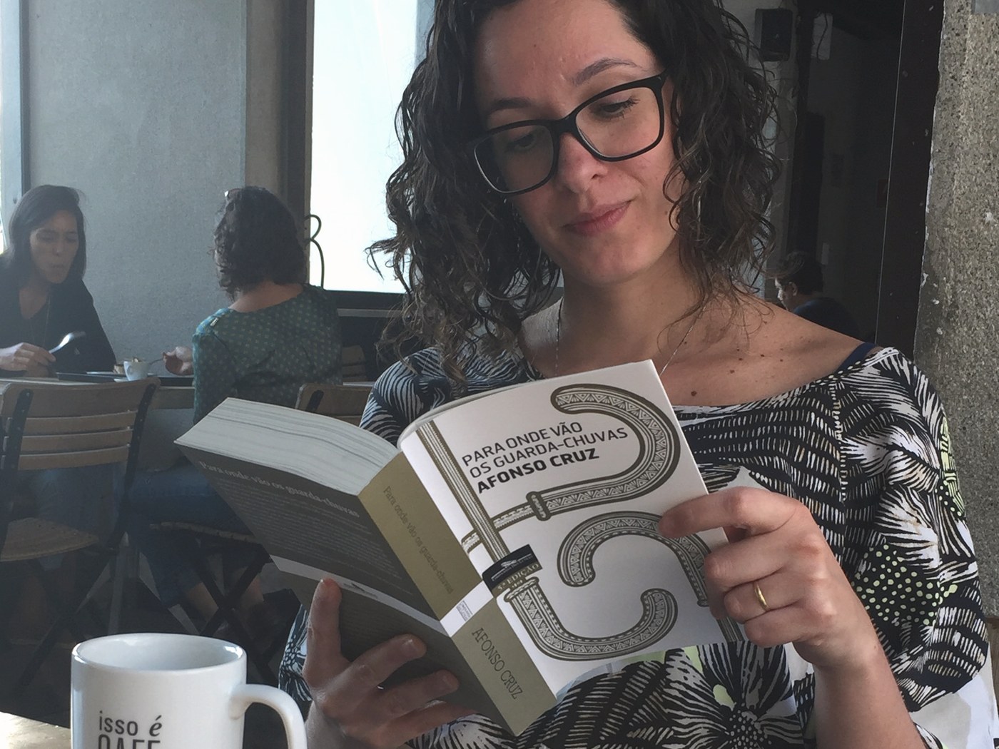 Mirella lendo à mesa com uma xícara de café